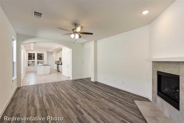 unfurnished living room with ceiling fan, a tile fireplace, and hardwood / wood-style floors