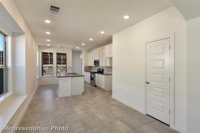 kitchen with white cabinetry, a center island with sink, stainless steel appliances, decorative backsplash, and sink