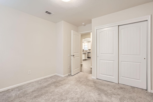 unfurnished bedroom with light carpet, a closet, and a textured ceiling