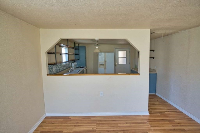 kitchen featuring white refrigerator with ice dispenser, baseboards, wood finished floors, and a textured wall