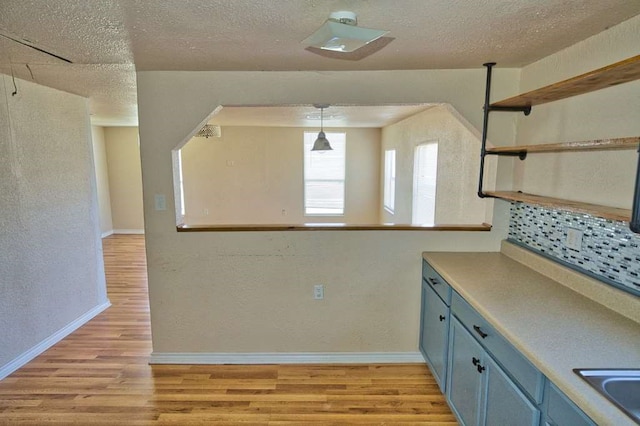 kitchen featuring light wood finished floors, open shelves, a textured ceiling, blue cabinets, and baseboards