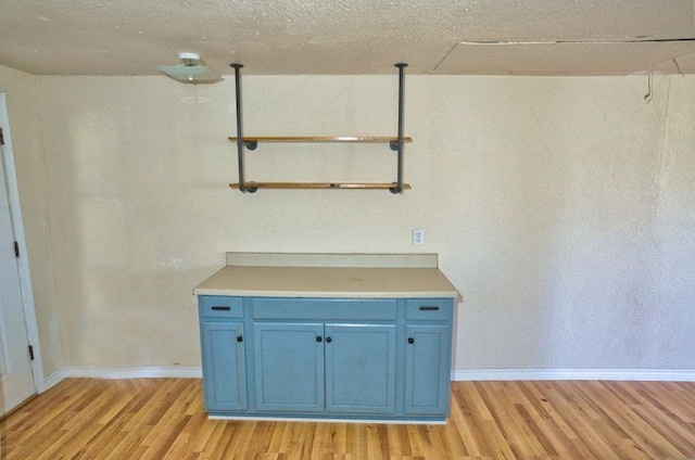 interior space featuring blue cabinets, light wood-type flooring, light countertops, and baseboards