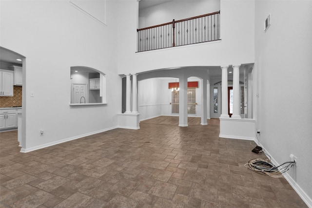 unfurnished living room featuring a towering ceiling and ornate columns