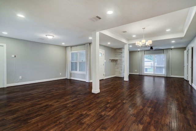 unfurnished living room with a raised ceiling, dark hardwood / wood-style flooring, ceiling fan with notable chandelier, and a stone fireplace