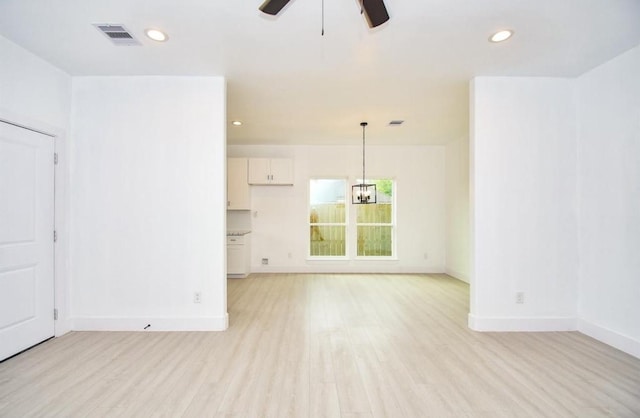 unfurnished living room with ceiling fan with notable chandelier and light hardwood / wood-style flooring