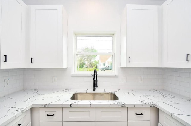 kitchen featuring decorative backsplash, white cabinets, light stone counters, and sink