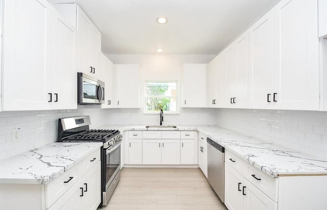 kitchen featuring appliances with stainless steel finishes, white cabinetry, sink, backsplash, and light stone counters