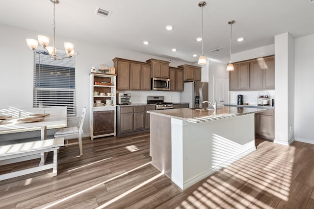 kitchen featuring appliances with stainless steel finishes, decorative light fixtures, dark hardwood / wood-style flooring, an island with sink, and an inviting chandelier