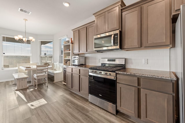 kitchen with tasteful backsplash, dark stone countertops, dark wood-type flooring, stainless steel appliances, and a chandelier