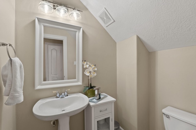 bathroom featuring toilet, a textured ceiling, vaulted ceiling, and sink