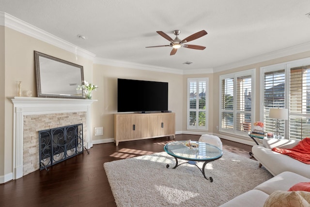 living room with crown molding, ceiling fan, dark hardwood / wood-style flooring, and a stone fireplace