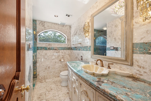 bathroom with tile walls, vanity, toilet, and tile patterned floors