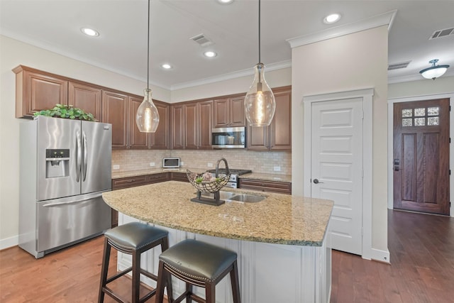 kitchen with light stone countertops, a kitchen island with sink, decorative backsplash, sink, and stainless steel appliances