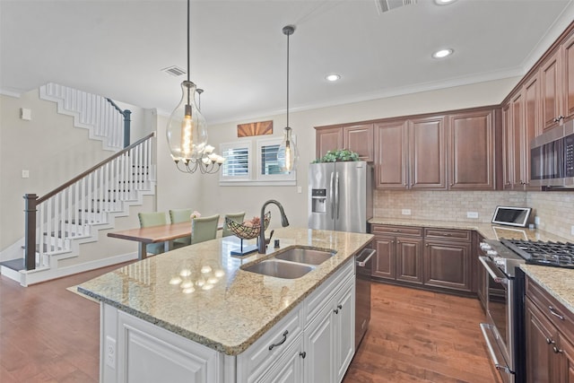 kitchen with white cabinetry, sink, ornamental molding, stainless steel appliances, and a center island with sink