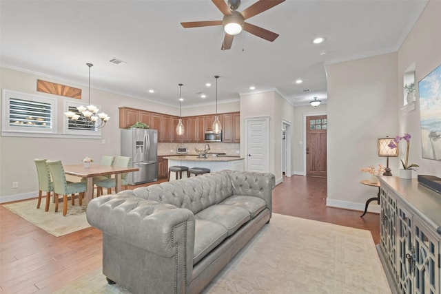 living room with crown molding, light hardwood / wood-style floors, ceiling fan with notable chandelier, and a wealth of natural light