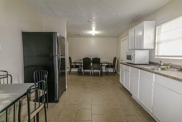 kitchen featuring black fridge, sink, light tile patterned floors, a textured ceiling, and white cabinets