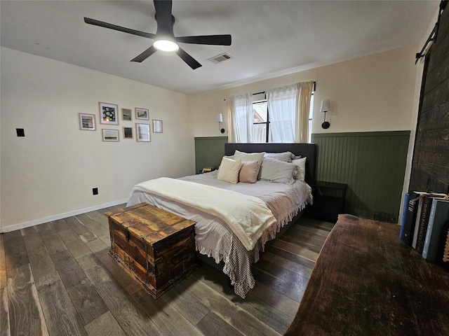 bedroom with ceiling fan, a barn door, and dark hardwood / wood-style flooring