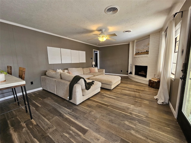 living room with a textured ceiling, dark hardwood / wood-style flooring, a fireplace, ornamental molding, and ceiling fan