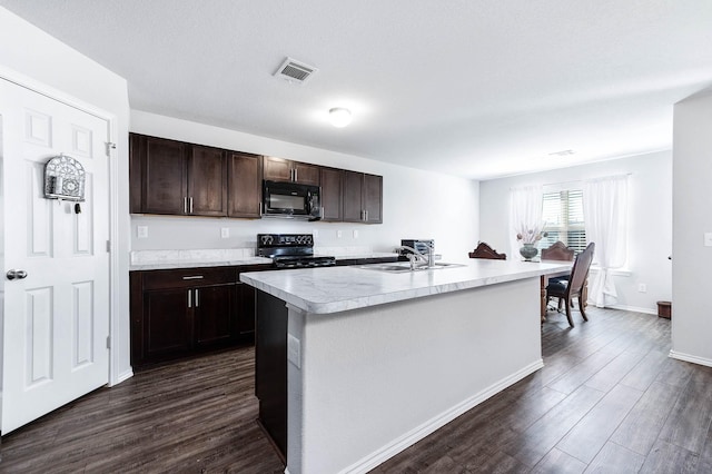 kitchen with dark brown cabinetry, black appliances, dark wood-type flooring, sink, and a center island with sink