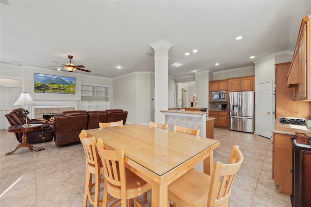 dining room featuring light tile patterned floors, built in shelves, ornamental molding, a tiled fireplace, and ceiling fan