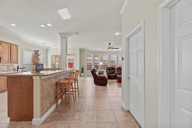 kitchen featuring a kitchen breakfast bar, ornamental molding, ceiling fan, light brown cabinets, and light tile patterned flooring