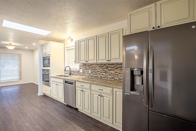 kitchen featuring light stone countertops, a skylight, stainless steel appliances, tasteful backsplash, and sink