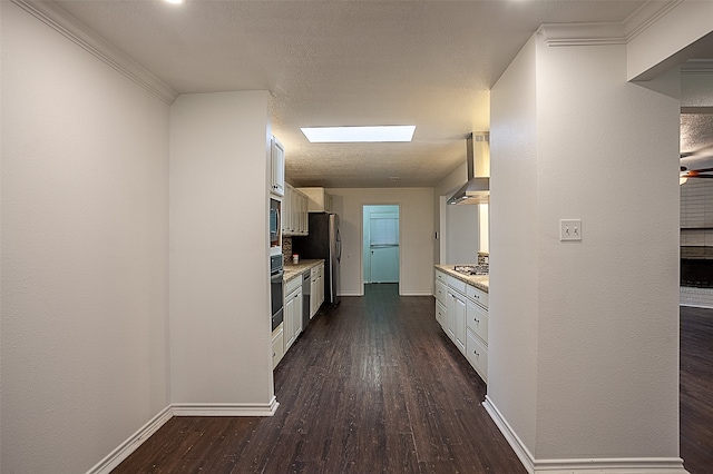 kitchen with white cabinetry, a skylight, dark wood-type flooring, stainless steel appliances, and wall chimney exhaust hood