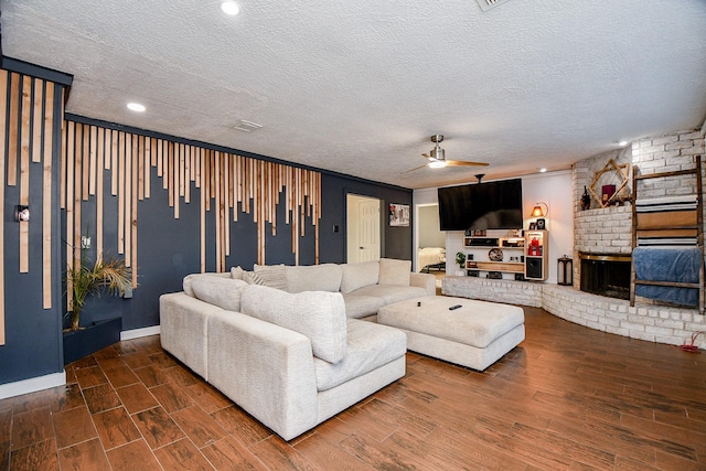 living room with ceiling fan, a large fireplace, a textured ceiling, and dark hardwood / wood-style flooring