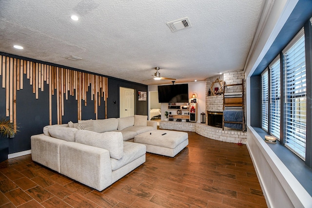 living room featuring a brick fireplace, a textured ceiling, and ceiling fan