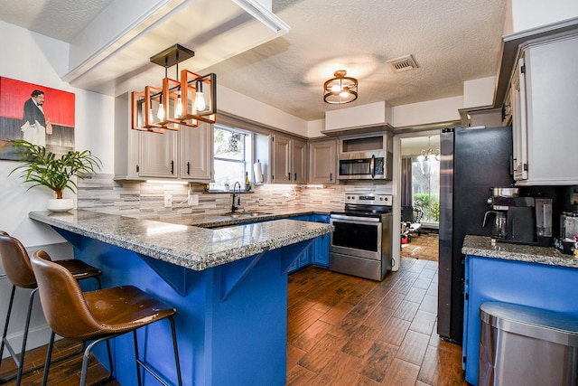 kitchen with appliances with stainless steel finishes, decorative light fixtures, backsplash, a kitchen bar, and kitchen peninsula