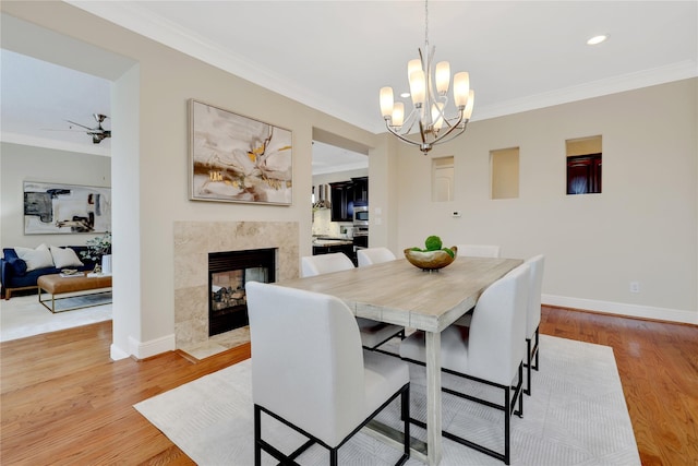 dining space featuring light hardwood / wood-style flooring, ceiling fan with notable chandelier, crown molding, and a tile fireplace