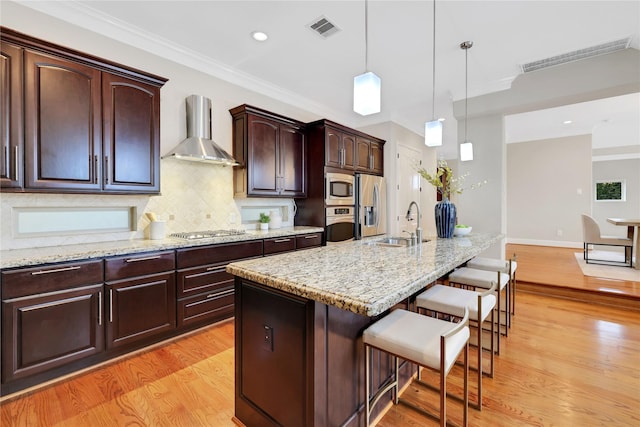 kitchen featuring tasteful backsplash, wall chimney range hood, a breakfast bar, a kitchen island with sink, and stainless steel appliances