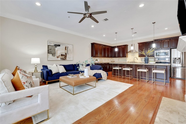 living room featuring ceiling fan, sink, crown molding, and light hardwood / wood-style floors