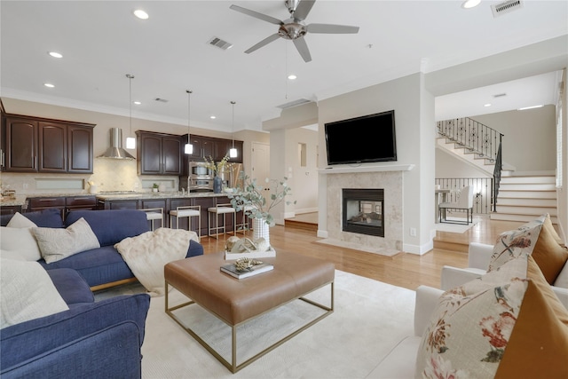 living room featuring ceiling fan, crown molding, a fireplace, and light hardwood / wood-style flooring