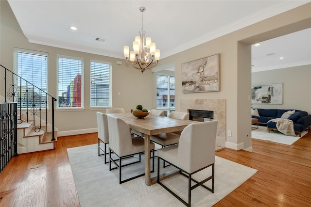 dining space featuring light hardwood / wood-style floors, a high end fireplace, crown molding, and an inviting chandelier