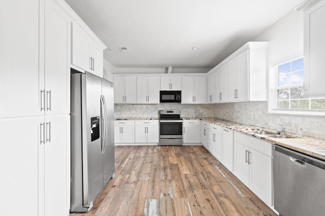 kitchen featuring stainless steel appliances, backsplash, light stone countertops, white cabinets, and sink