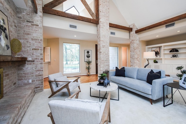 living room featuring high vaulted ceiling, a brick fireplace, light hardwood / wood-style flooring, and ornate columns