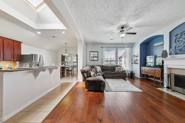 tiled living room featuring ceiling fan, a textured ceiling, lofted ceiling, and a tiled fireplace