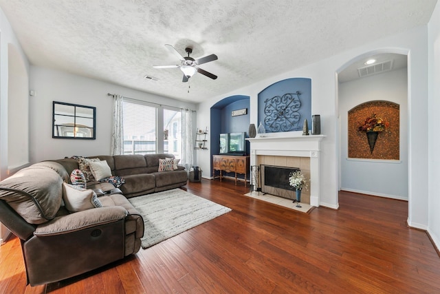 living room featuring ceiling fan, a fireplace, dark hardwood / wood-style flooring, and a textured ceiling