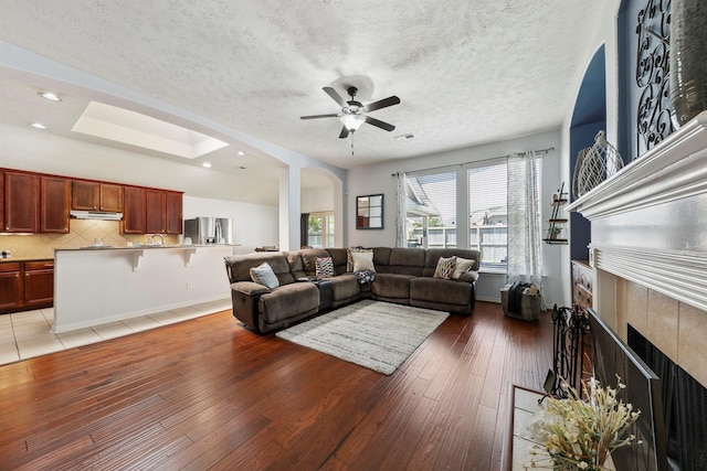 living room featuring ceiling fan, a skylight, a tile fireplace, and hardwood / wood-style floors