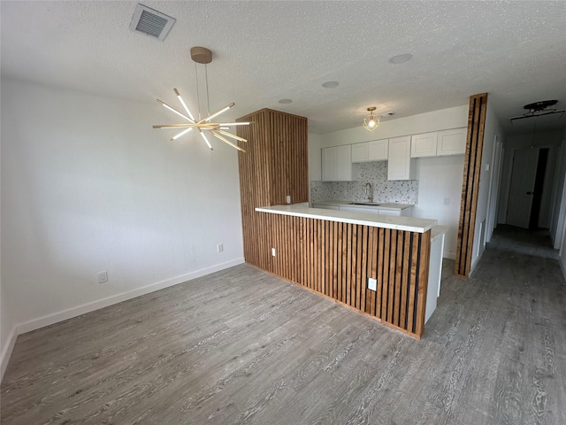 kitchen with hardwood / wood-style floors, kitchen peninsula, sink, an inviting chandelier, and white cabinets