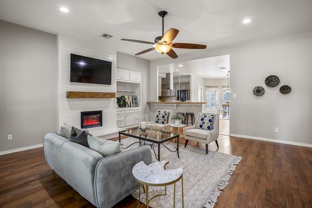 living room featuring ceiling fan, built in shelves, dark hardwood / wood-style floors, and a fireplace