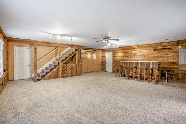 unfurnished living room with wood walls, rail lighting, carpet, and indoor bar