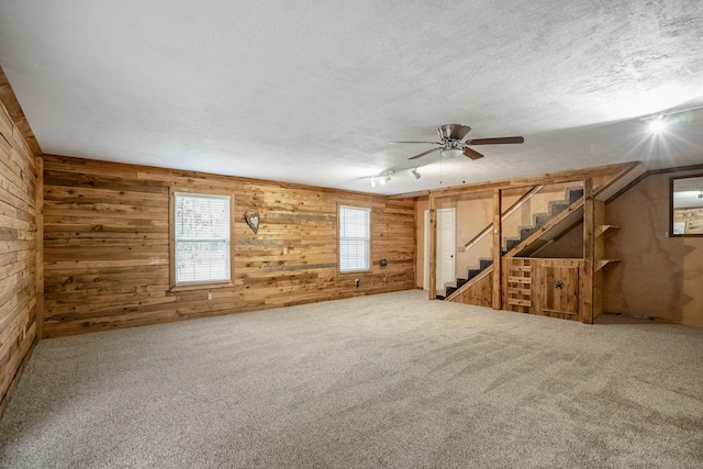 empty room featuring a textured ceiling, ceiling fan, carpet floors, and wooden walls