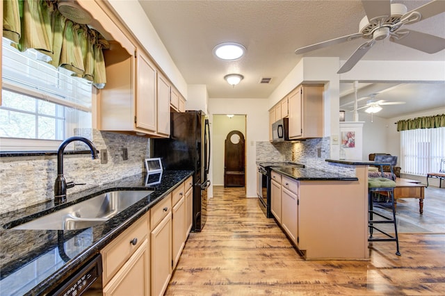 kitchen with sink, a kitchen breakfast bar, light wood-type flooring, dark stone countertops, and black appliances