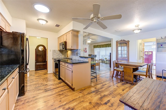 kitchen featuring light hardwood / wood-style floors, a kitchen bar, dark stone counters, and black appliances