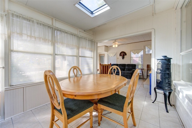 tiled dining room featuring ceiling fan, wood walls, and a skylight