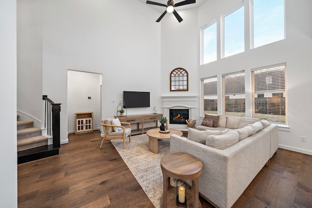 living room with a towering ceiling, dark wood-type flooring, and ceiling fan