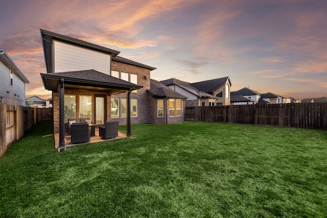 back house at dusk with an outdoor living space, a patio area, and a lawn