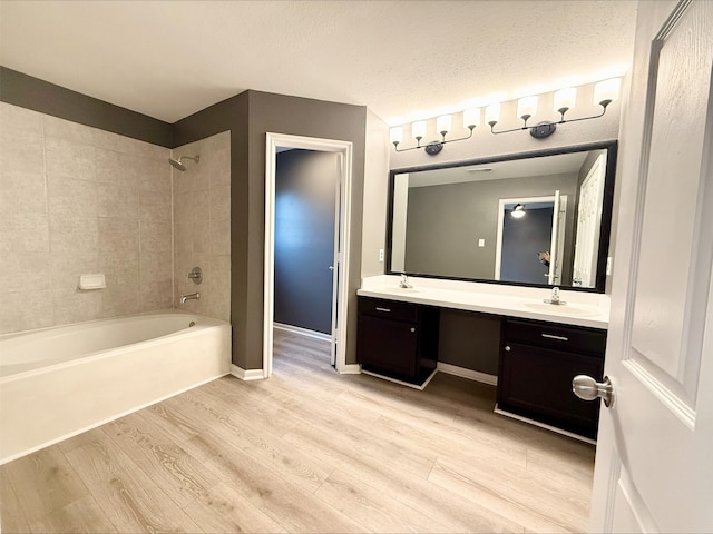 bathroom with hardwood / wood-style flooring, a textured ceiling, vanity, and tiled shower / bath